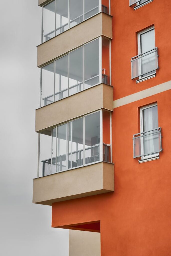Close-up of a modern apartment building facade with glass balconies and orange walls.