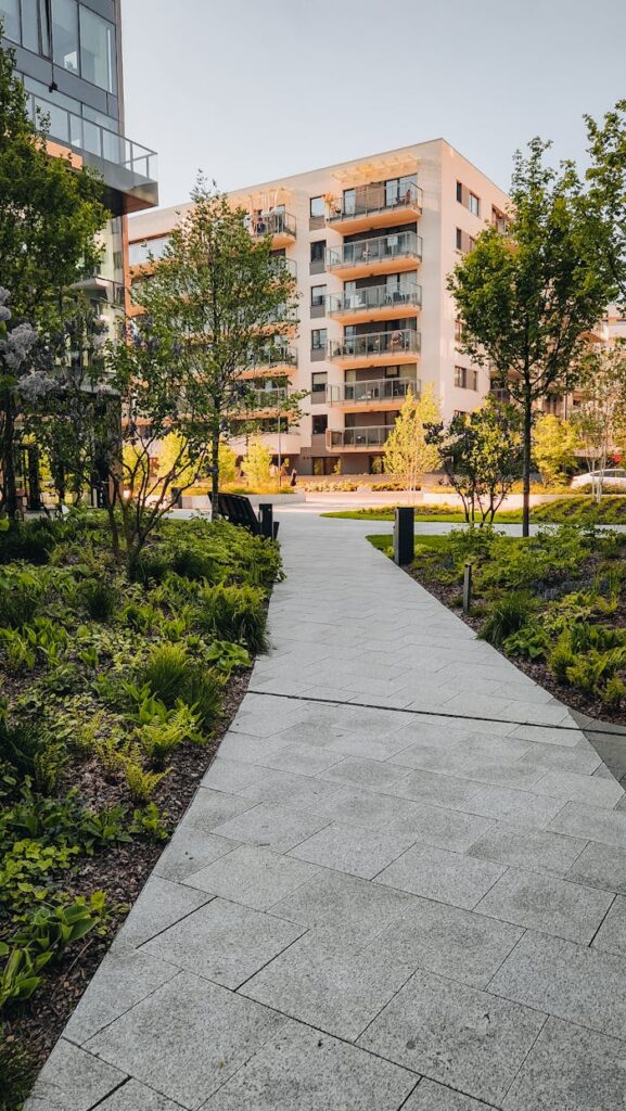 A tranquil modern residential pathway surrounded by trees and greenery with modern apartments in the background.