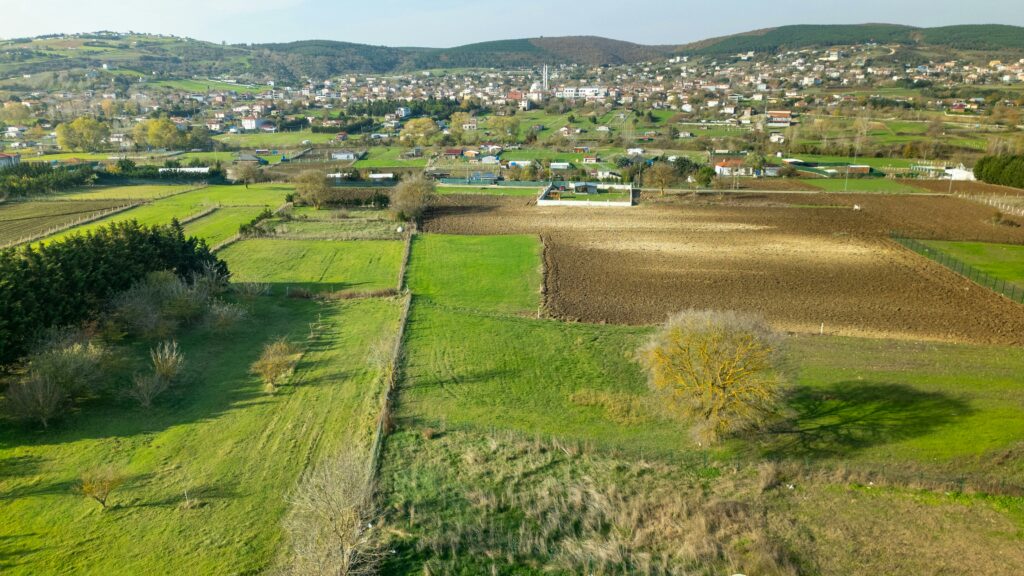 Aerial shot showcasing lush green fields and quaint Turkish village in spring.