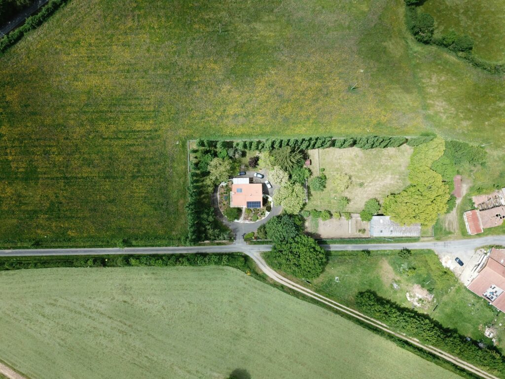pexels-photo-8368955-8368955 Drone shot showcasing a rural farmhouse surrounded by lush greenery in Pays de la Loire, France.